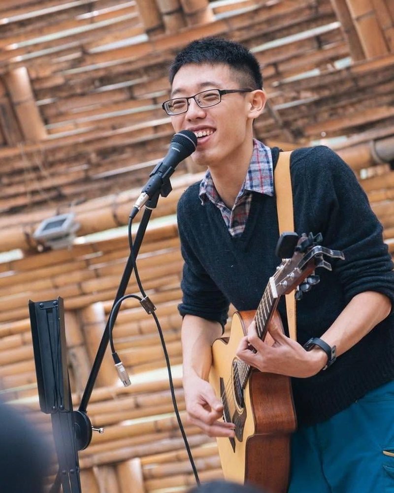 Awei playing guitar and singing under a bamboo shelter