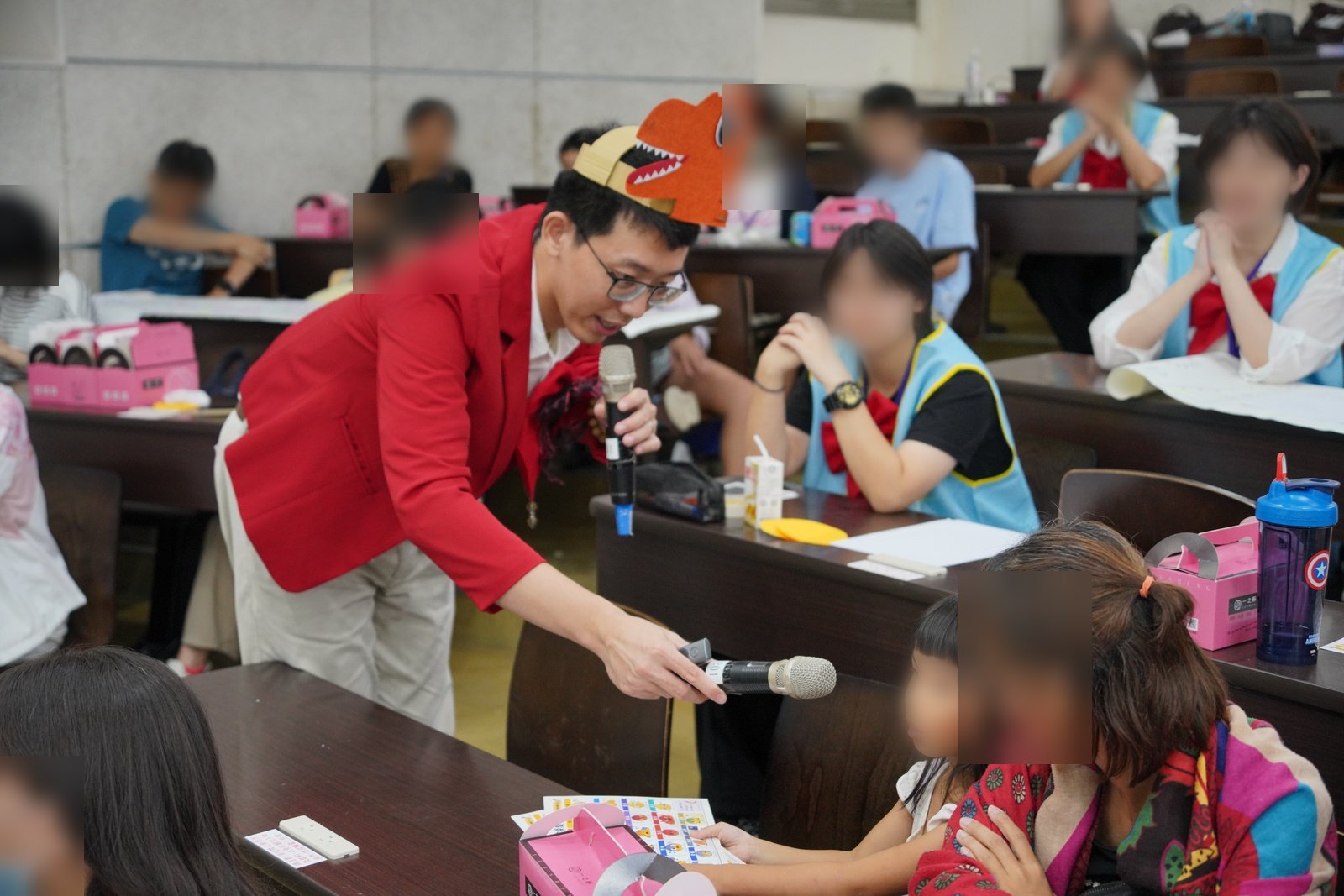 講師彎腰把麥克風遞給座位上的孩子，旁邊大人和孩子一起聽