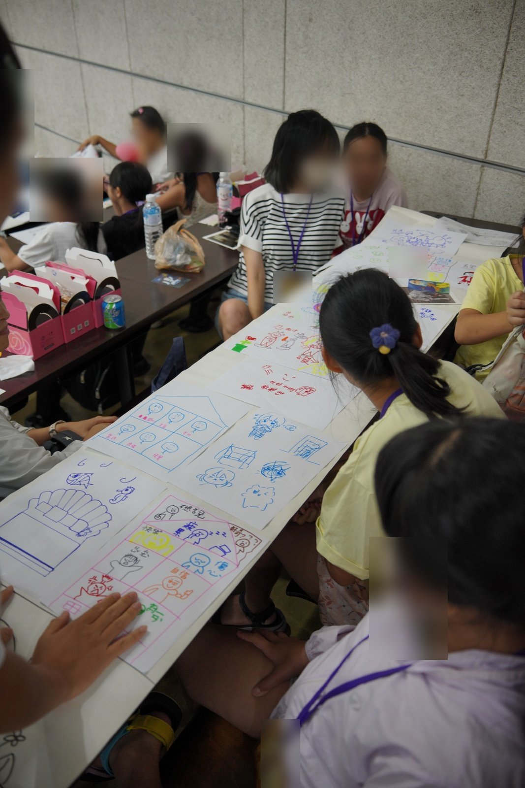 長桌上一張接一張排著孩子畫的情緒房間，孩子們圍坐在旁邊看